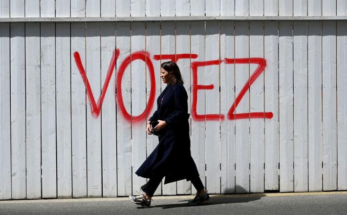 A woman walks past graffiti on a fence that reads, 'Vote', in Paris, France.Photographer: Emmanuel Dunand/AFP/Getty Images