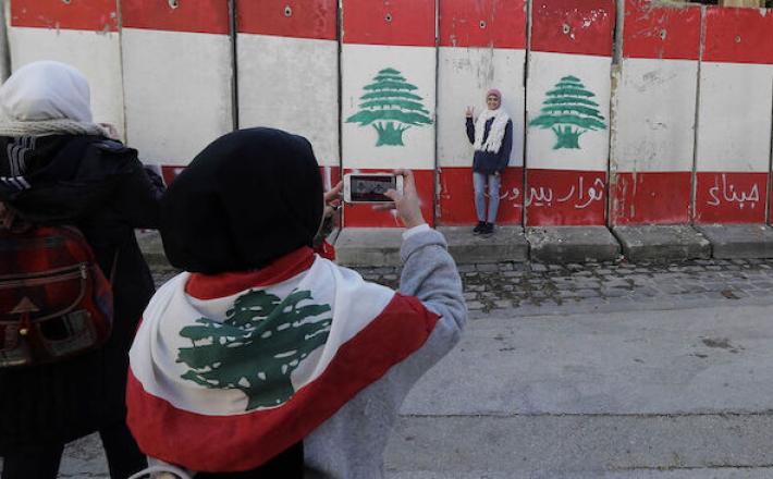 A woman takes a photograph of another standing in front of a wall of cement blocks, set up by Lebanese security forces to bar a street leading to the parliament building, Beirut, Lebanon, Jan. 24, 2020. - Joseph Eid/AFP via Getty Images